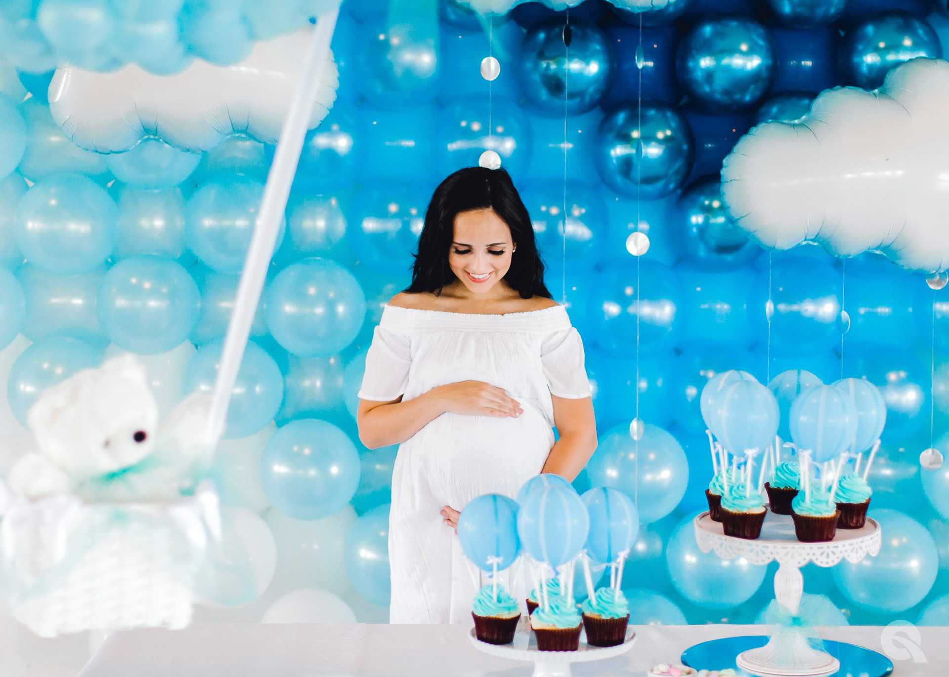 Eine Frau in einem blauen Shirt vor Ballons und Babysachen.
